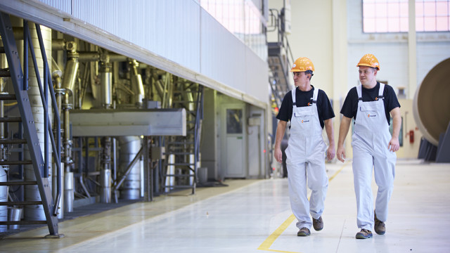 Two men walk beside a paper-making machine.