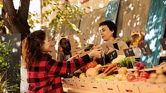 Women standing in front of selected fruit in corrugated boxes, buying fruit.