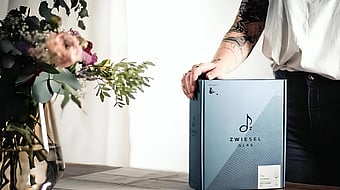 A person is holding a package of Zwiesel Glas glassware on a table.