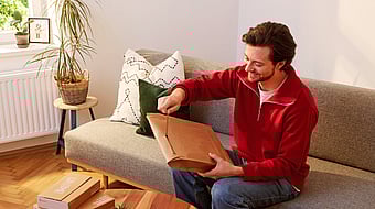 man in red jumper sitting on a sofa opening a package