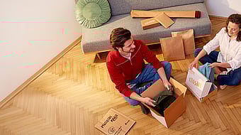 man and woman sitting cross legged opening corrugated packages