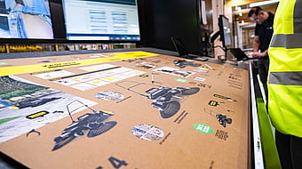 man in hi-vis jacket overlooking a machine printing imagery and text onto a cardboard box