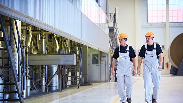 Two men walk beside a paper-making machine.